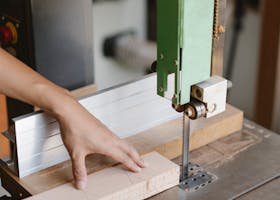 Crop unrecognizable woodworker sawing wooden plank with band saw with sharp blade in daytime